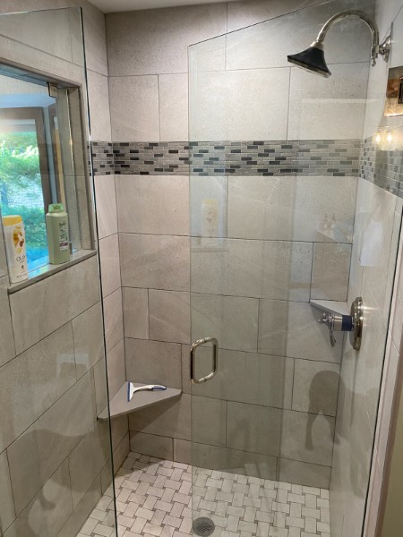 Walk-in shower with cream tile and a colorful glass mosaic accent band